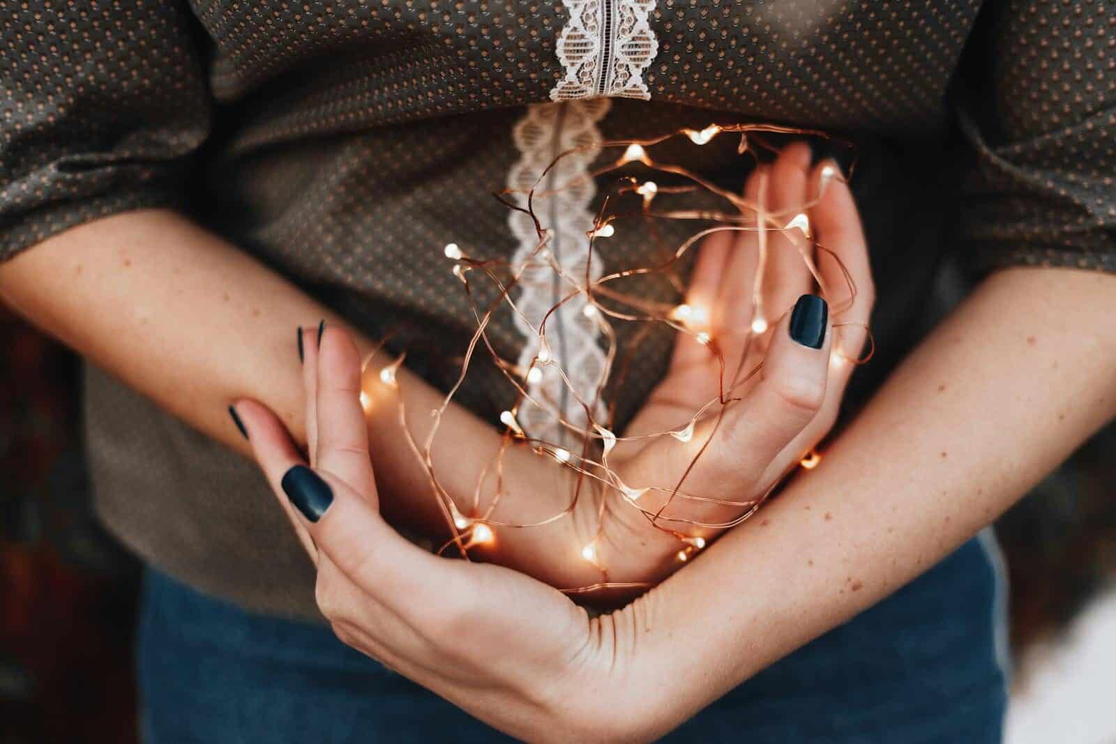 Close-up of a woman's hands gently holding glowing string lights, creating a warm festive vibe.